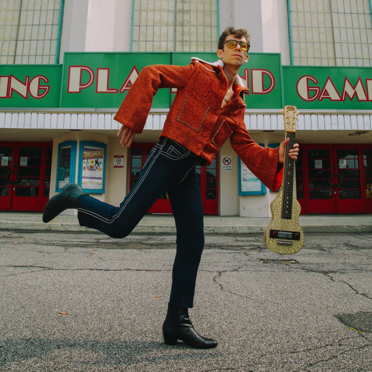 Sam Kogon mid-stride with a guitar outside Playland